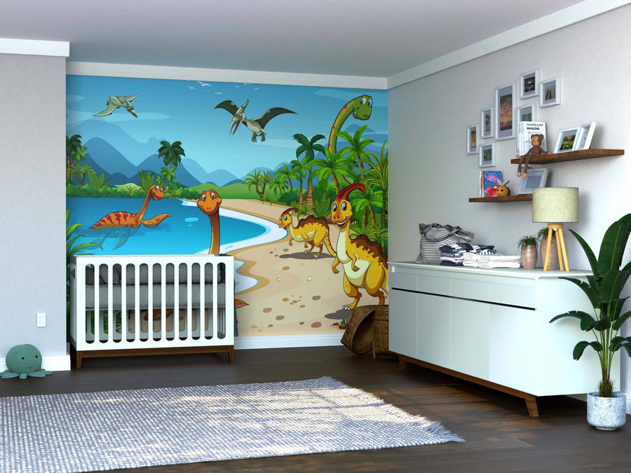 A nursery displays a crib by the wall with the Dinos at the Beach Wall Mural, featuring dinosaurs by water, mountains, and palm trees. The space includes a white dresser, plant, floating toy shelves, framed photos, and wood flooring.