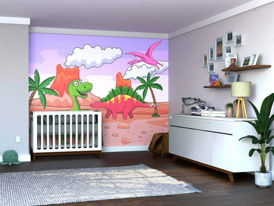 A nursery with wooden floors and white furniture features the Dino Day Wall Mural—a colorful peel and stick design of cartoon dinosaurs, palm trees, and mountains beneath a pink and purple sky. Shelves, plants, and photo frames decorate the right side.