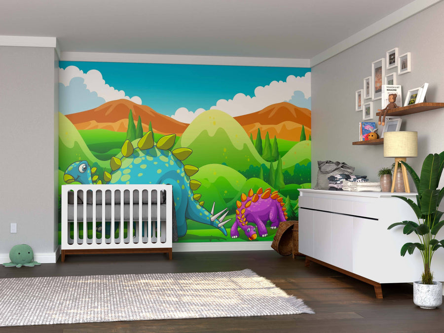 A baby nursery with a crib, dresser, and plant features the Dino Stroll Wall Mural of cartoon dinosaurs and green hills behind the crib. Framed photos and baby supplies are on the dresser; a plush turtle toy sits on the floor.