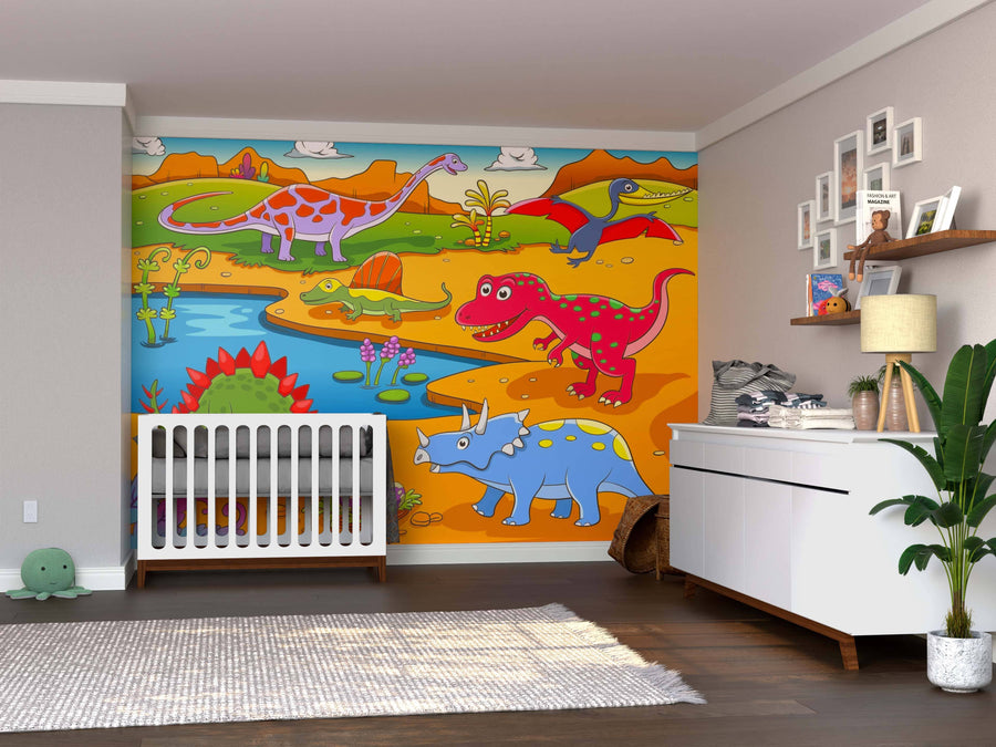 A nursery room with the Dino Valley Wall Mural, a colorful peel and stick mural featuring cartoon dinosaurs and a prehistoric landscape. The room has a white crib, dresser with baby items, wooden flooring, potted plant, and plush toy.