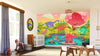 A bright nursery features the Dinosaurs by the River Wall Mural with cartoon dinosaurs in a colorful prehistoric scene of trees and a pond. The room includes a crib, rocking horse, toy blocks, basket, light wood flooring, and a rug.