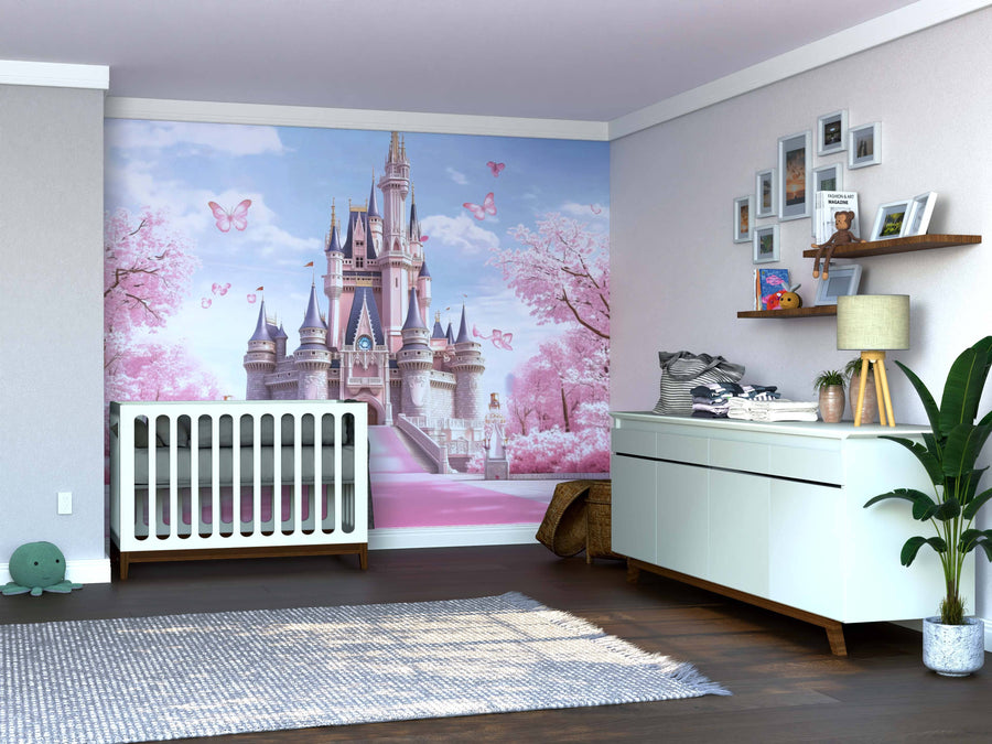 A nursery with a white crib, dresser, and shelves features the Enchanted Pink Castle Wall Mural with butterflies and trees. A gray rug covers the wooden floor, accented by toys, plants, and framed pictures on walls and shelves.