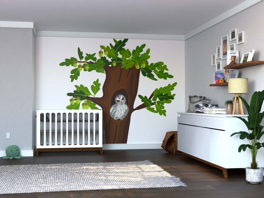 A nursery features a white crib, a dresser with a nearby plant, toy-filled shelves, and the Hollow Nest Owl Wall Mural—a peel and stick mural showcasing a tree with green leaves and an owl on the wall.
