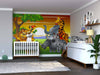 A nursery room with a crib and dresser features wood flooring, a large plant, and framed photos above the changing table. The wall showcases the colorful Jungle Wildlife Joy Wall Mural with cartoon jungle animals.