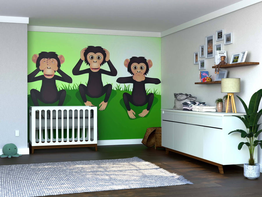 A nursery features the Monkeys Wall Mural, a custom peel and stick design of three cartoon monkeys making "see no evil, hear no evil, speak no evil" gestures on a green wall. The room also has a white crib, dresser, toys, plants, and framed photos on shelves.