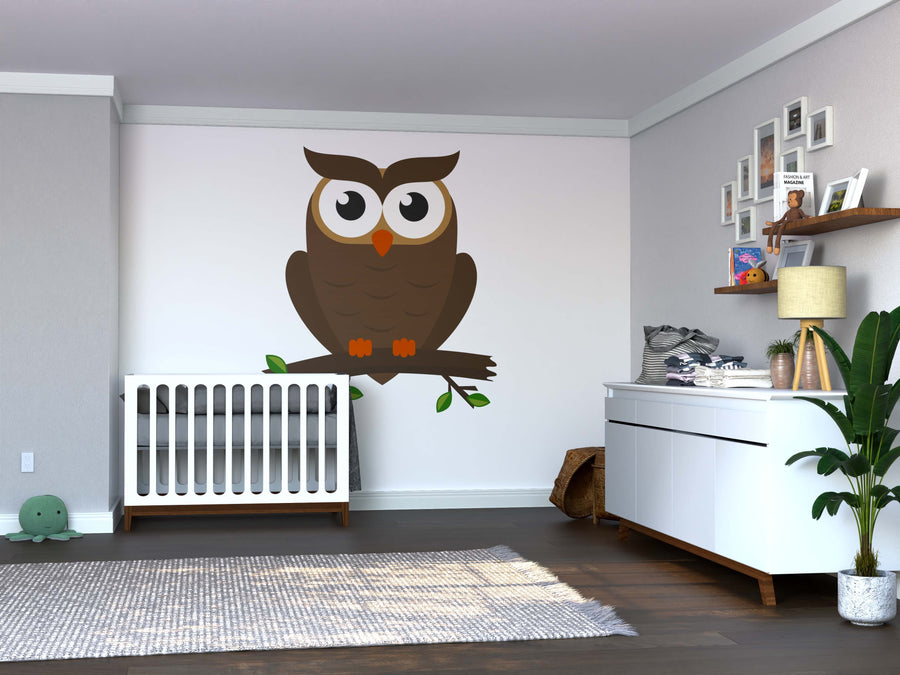 A modern nursery with gray walls features a white crib, a dresser with baby items, and the Night Guardian Wall Mural enamelled on one wall. Framed pictures, a tall green plant, and soft natural light complete this cozy space.