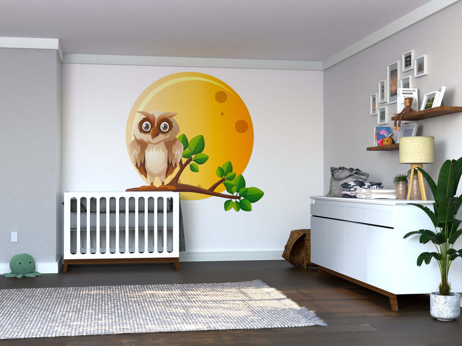 A nursery with a white crib, dresser, baby essentials, toys, framed photos, a green plant, and a soft rug on the wooden floor features the Night Owl Wall Mural—an owl on a branch in front of a yellow moon.