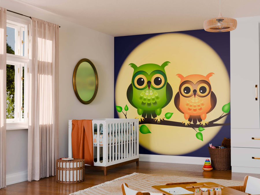 A nursery with a white crib, wicker ottoman, round mirror, and sheer-curtained windows showcases the Owls and Full Moon Wall Mural, which depicts two cartoon owls perched on a branch in front of a glowing moon.