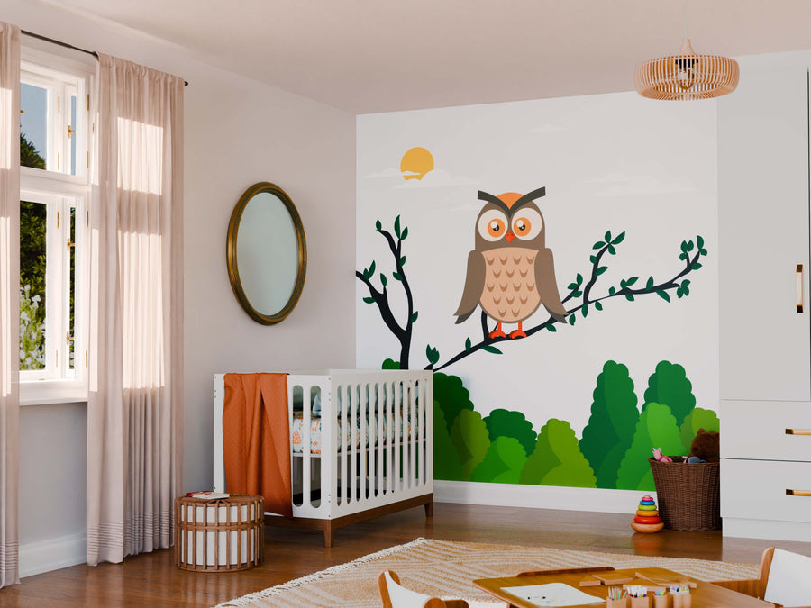 A cozy nursery with wooden floors features a white crib, wicker ottoman, and play area. The wall displays the Owl Perched on a Tree Wall Mural with green trees and a yellow sun, illuminated by light through sheer curtains.