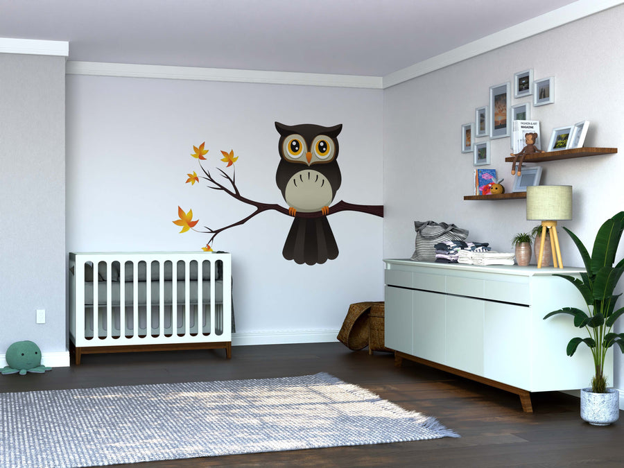 A nursery room with a white crib, dresser with decor and plants, and the Owl on A Branch Wall Mural featuring a cartoon owl among autumn leaves. The space has wooden floors, light walls, and framed photos on shelves.