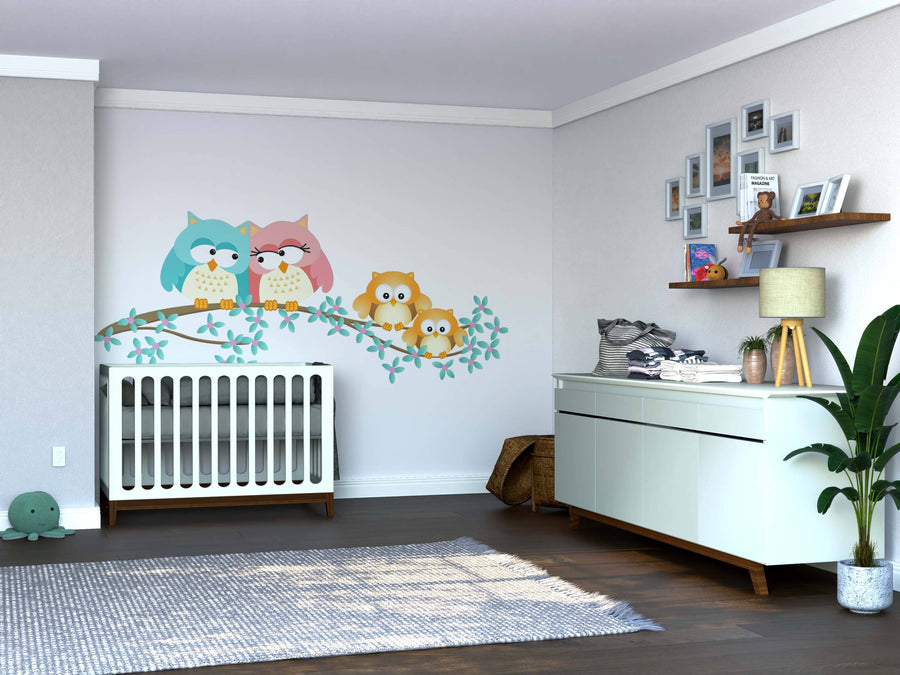 A modern nursery with a white crib, dresser, and the Owls on Flowered Branch Wall Mural as a colorful focal point. Above the dresser is a shelf with photos and toys. A potted plant, basket, and green turtle toy rest on the dark wood floor.