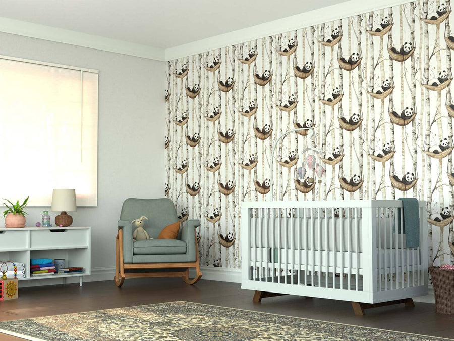 A bright nursery features a white crib, green armchair with a teddy bear, and shelves of books and toys. The walls are adorned with the Panda Hammock Haven Wall Mural, and a patterned rug covers the wood floor beneath the window.