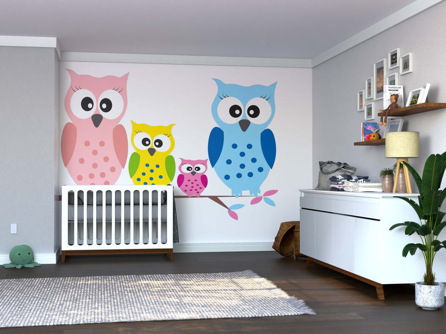 A nursery with a crib, dresser, shelf with decor, hardwood floors, gray rug, leafy plant, and a large custom peel-and-stick "Pastel Birds on Branch Wall Mural" featuring four colorful cartoon owls perched on a branch.