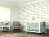 A bright nursery features a crib, rocking chair with teddy bear, bookshelf, lamp, large window, and a patterned rug. The wall showcases playful horizontal stripes with colorful floral designs from the Pastel Floral Harmony Wall Mural.