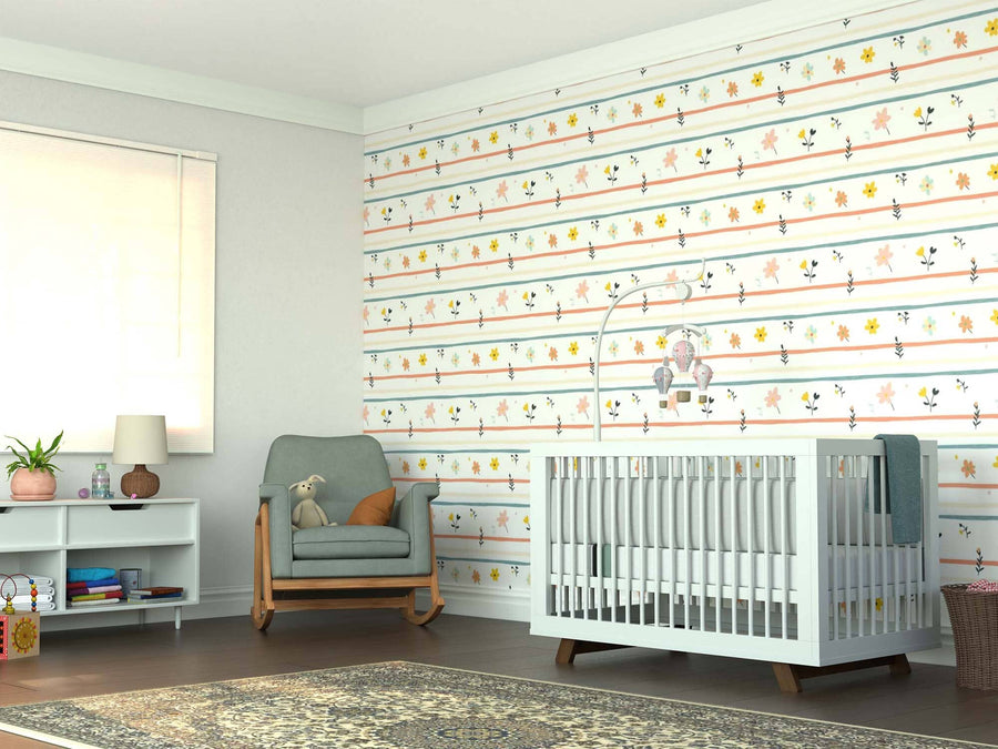 A bright nursery features a crib, rocking chair with teddy bear, bookshelf, lamp, large window, and a patterned rug. The wall showcases playful horizontal stripes with colorful floral designs from the Pastel Floral Harmony Wall Mural.