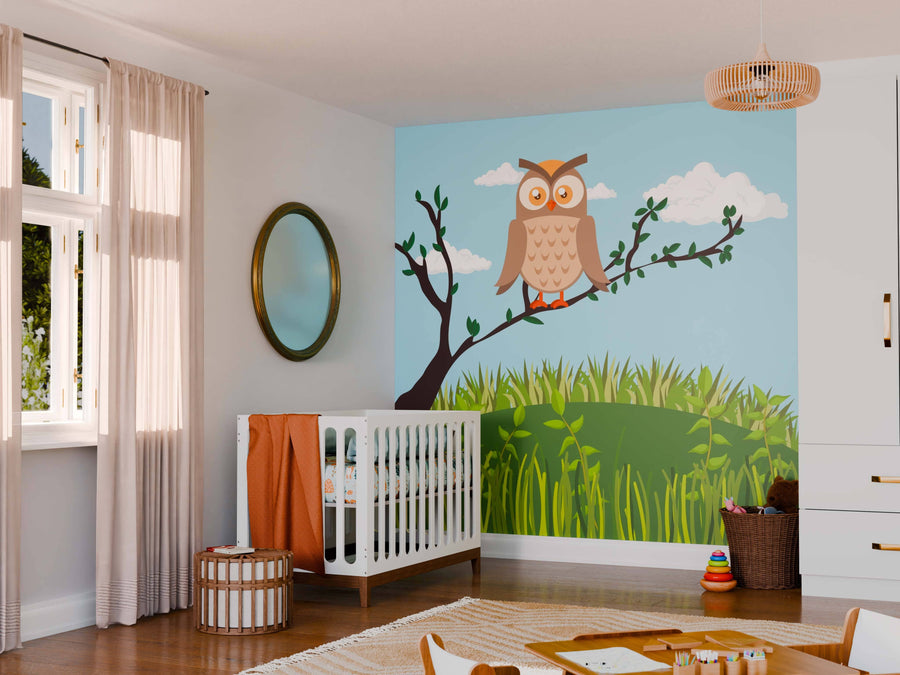 A nursery features a white crib with orange bedding, a round mirror, and the Peaceful Owl Wall Mural showing an owl on a tree branch with grass and clouds. Natural light fills the room as toys rest on the wooden floor rug.