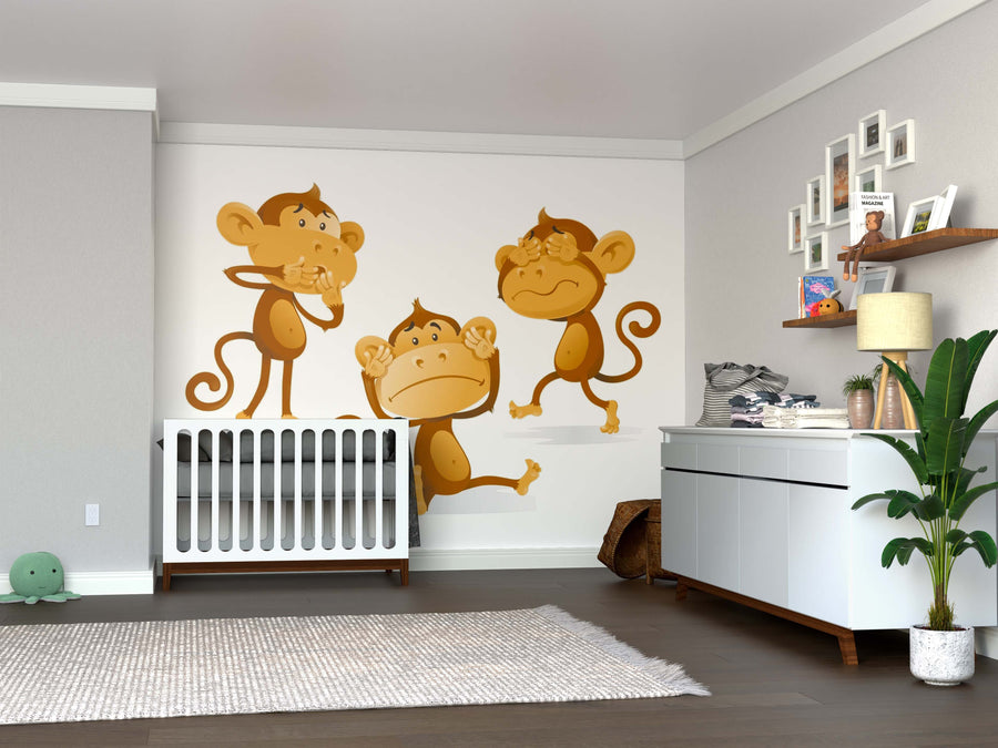 A nursery featuring a white crib, the Playful Monkeys Wall Mural with three cartoon monkeys, a dresser topped with a plant and baby items, wooden floor, framed photos on the wall, and a plush turtle on the floor.