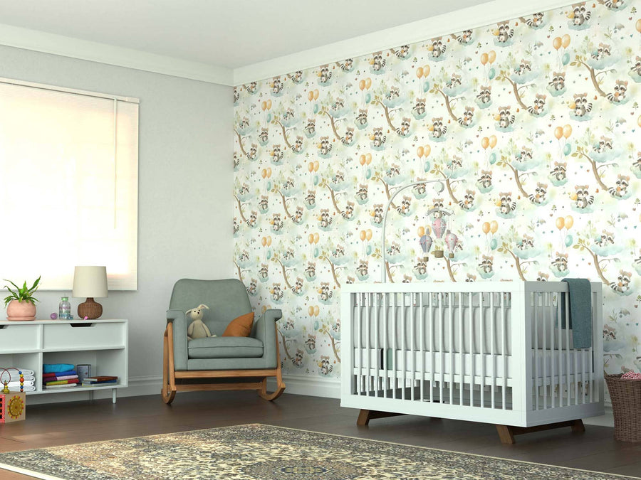 A cozy nursery with the Raccoon Wonderland Wall Mural, a white crib, green armchair with a teddy bear, small shelf with toys and books, lamp, window with shade, and a patterned rug on the wooden floor.