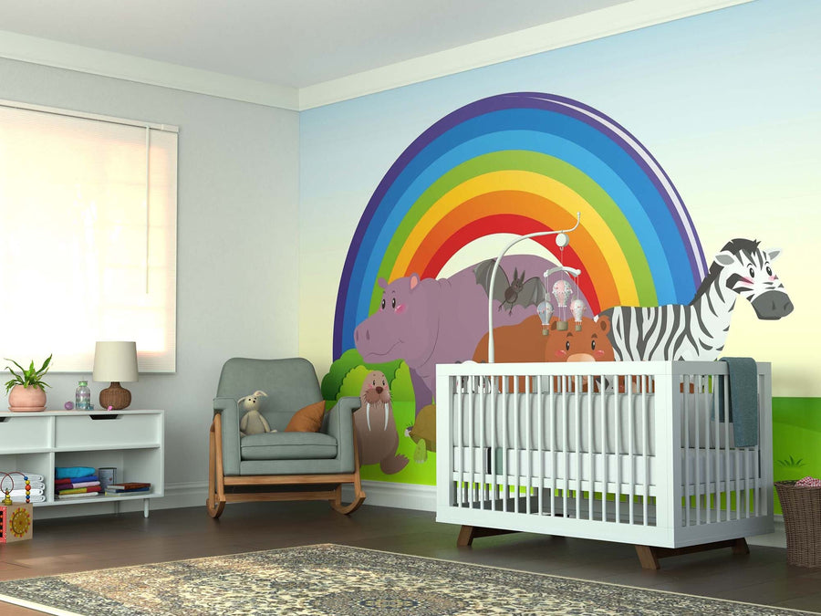 A nursery features a crib, plush toys, and the Rainbow Wildlife Wall Mural with cartoon animals. A white shelf for books and decor stands by a cushioned chair, window, and patterned rug on dark wood floors.