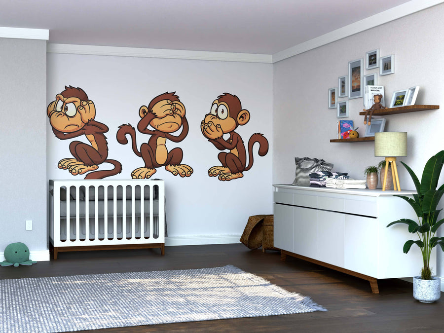 A nursery with a white crib and dresser features the See No Evil Monkeys Wall Mural. Removable wallpaper adds charm, while plush turtles, shelves with books, photos, a basket, and a potted plant complete the cozy space.