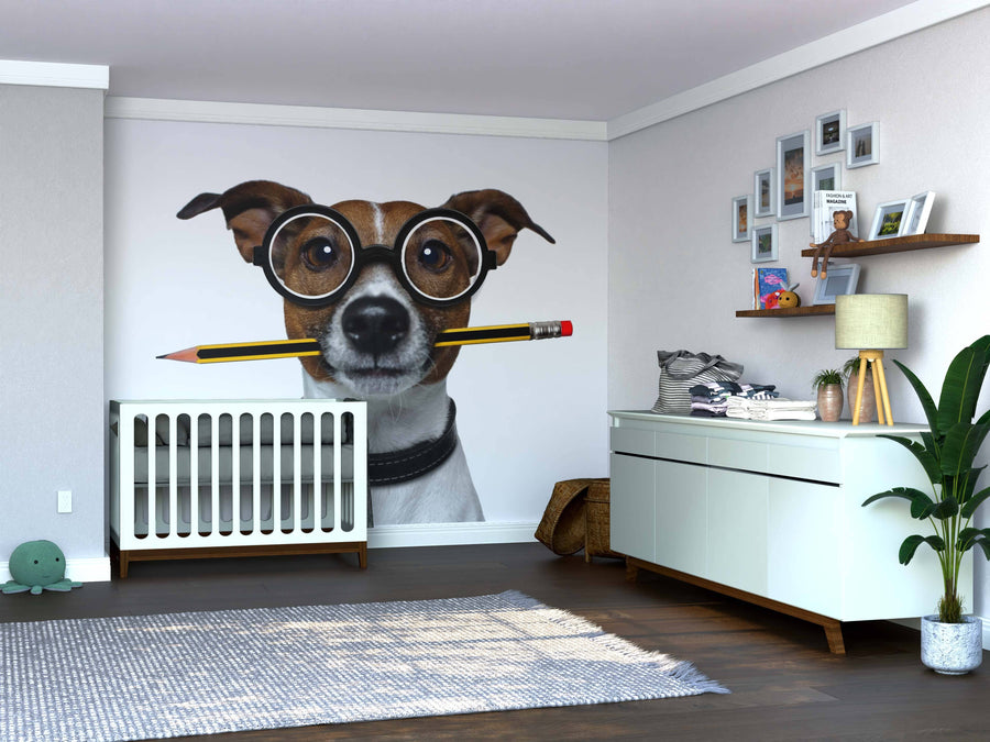 The cozy, bright nursery features the Smart Pup Wall Mural showing a dog with glasses and pencil, plus a white crib, dresser, shelves with photos, green plant, toys on a grey rug, and wooden floors.