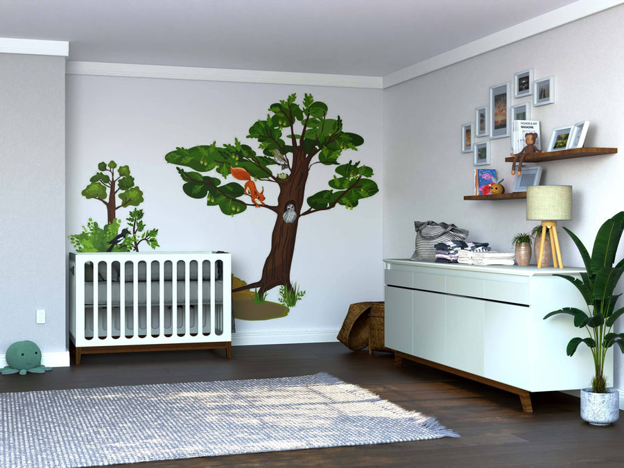 A modern nursery with a white crib, Squirrel and Owl Wall Mural of forest animals and trees, a changing table with supplies, a gallery wall, houseplants, and a soft gray rug on dark wood floors. Warm, inviting, organized space with natural light.