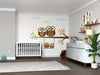 A modern nursery with a white crib and dresser features the Swinging Owl Family Wall Mural—peel and stick accents in neutral tones with colorful owls on branches—plus baby supplies and a large green plant.