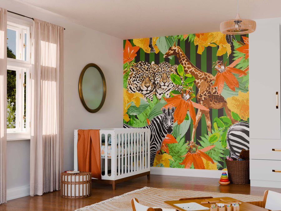 A nursery has the Tropical Wildlife Wall Mural with a leopard, giraffe, zebra, and tropical leaves. It features a white crib with orange bedding, a wicker basket, round mirror, and large window with sheer curtains.