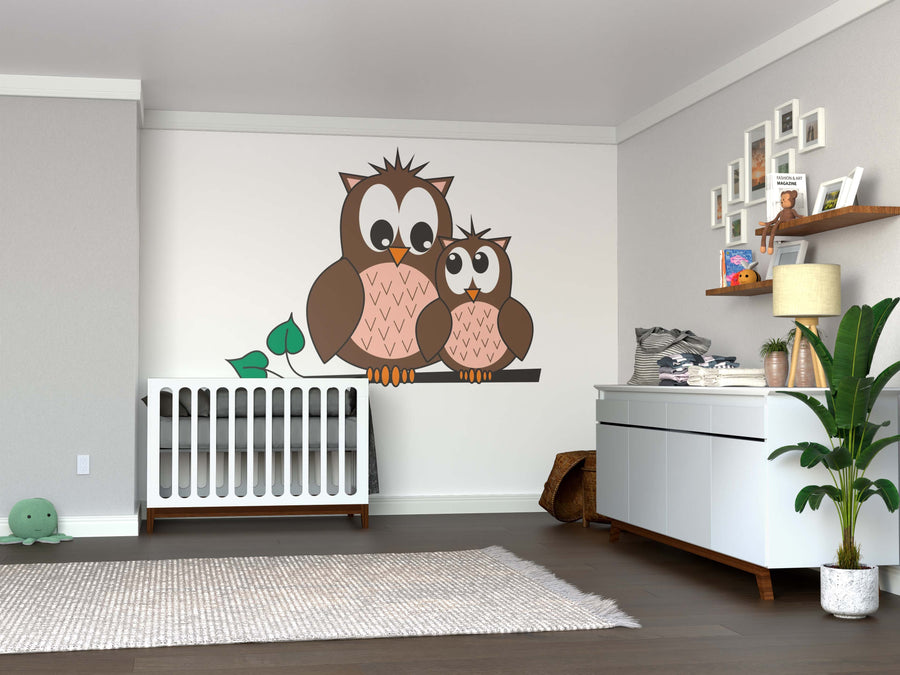 A cozy nursery featuring the Two Cute Owls Wall Mural, a crib, white dresser with baby supplies, floating shelf with toys and frames, green potted plant, woven basket, plush turtle, and a beige rug on wooden flooring.