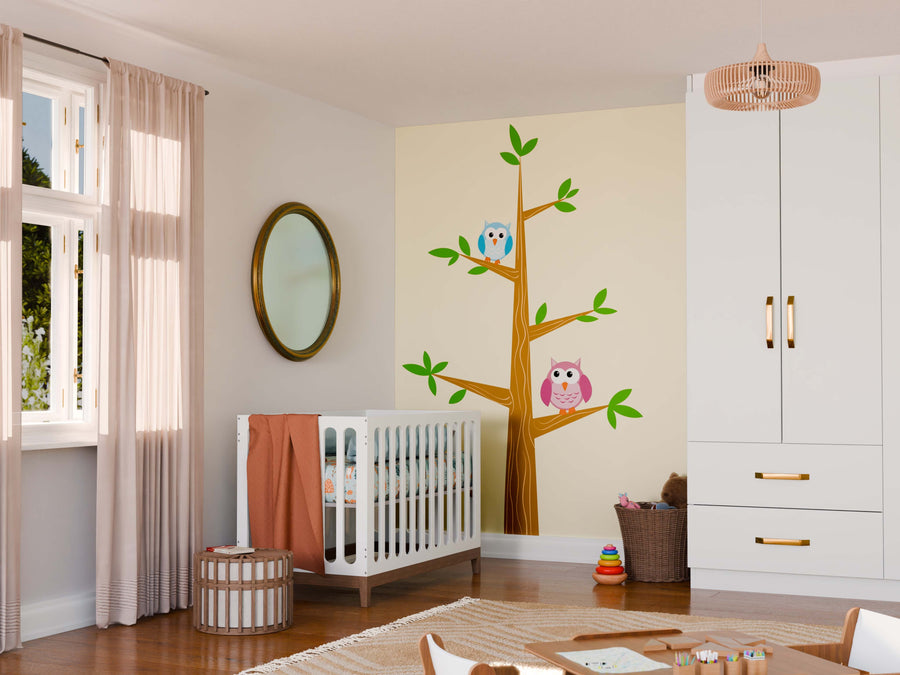 A cozy nursery with a white crib, round mirror, and wicker basket. The wall features the Two Owls on the Tree Wall Mural—one blue and one pink owl on branches. Soft curtains frame the window; toys are stacked in the corner.