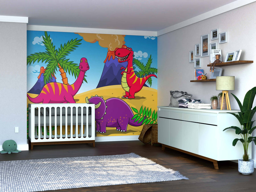 A nursery features the Volcano Valley Adventures Wall Mural with colorful cartoon dinosaurs and volcanoes. A white crib and dresser sit against the mural, accented by framed photos, a plush toy, and a leafy green plant.