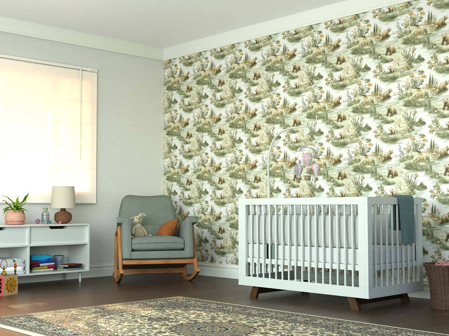 A bright nursery showcases a white crib with a mobile, gray armchair with teddy bear, and a small white shelf. The Wilderness Bears Wall Mural adds charm, while sunlight highlights the woven rug on the dark wood floor.