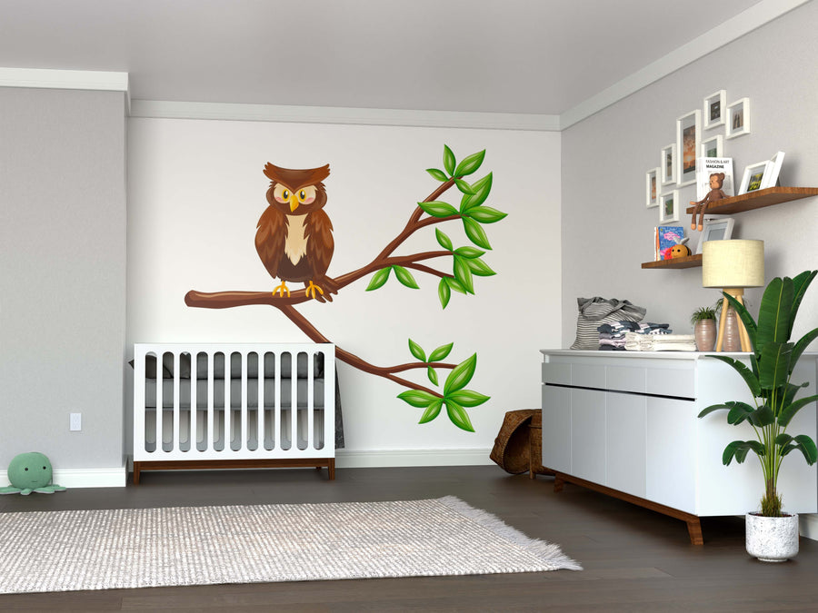 A nursery with a crib, dresser with a plant, shelf, light walls, hardwood floors, toys, framed photos, and gray rug. Above the crib, the Wise Owl on Branch Wall Mural adds charm and character to the space.