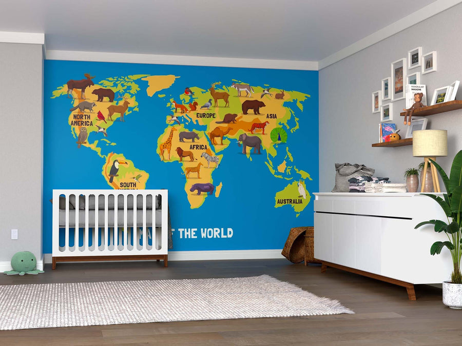 A nursery with a crib and dresser features the World Animal Map Wall Mural, displaying labeled continents and illustrated animals. Shelves hold toys and books, while a plant and basket sit on the wooden floor.