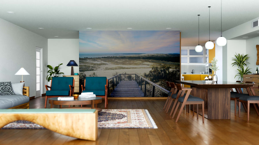A modern, open-concept living-dining area with wood floors and mid-century furnishings features the Oceanward Steps Wall Mural—a boardwalk to the ocean under a pastel sky. Rug, sofa, and kitchen can be seen in the background.
