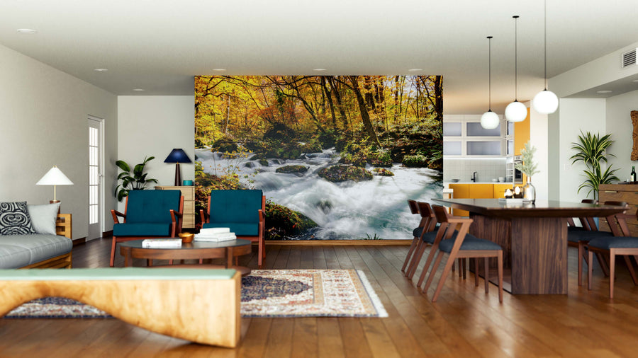 Modern open-plan living and dining room with wooden floors, teal chairs, a rug, and the Oirase Stream Wall Mural depicting a flowing autumn forest river; kitchen in background, pendant lights above dining table.