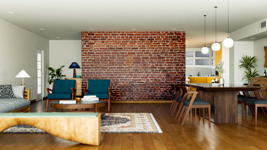 Modern open-plan living and dining area with an Old Brick Facade Wall Mural, wooden floors, dark green chairs, gray sofa, large dining table with chairs, pendant lights, indoor plants, and a kitchen with yellow cabinets in the background.