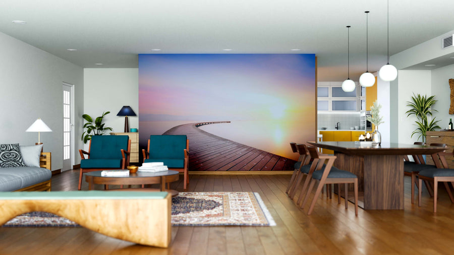 A modern living-dining space with wooden floors, green chairs, pendant lights, indoor plants, and the Pastel Pier Sunset Wall Mural creates a bright, airy contemporary vibe. The kitchen is visible for an open feel.