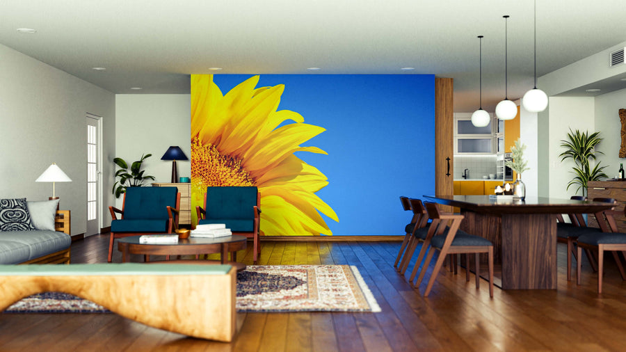 A modern open-plan living and dining room features wooden floors, stylish furniture, and the "Petals in the Sky Wall Mural," showcasing a sunflower against a blue background for a vibrant touch in the bright, neat space.