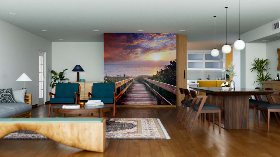 Modern open-concept living and dining area with wood floors, mid-century furniture, and a large Beach Boardwalk Wall Mural showing a vibrant sunset view. Contemporary decor and pendant lights complete this stylish space.