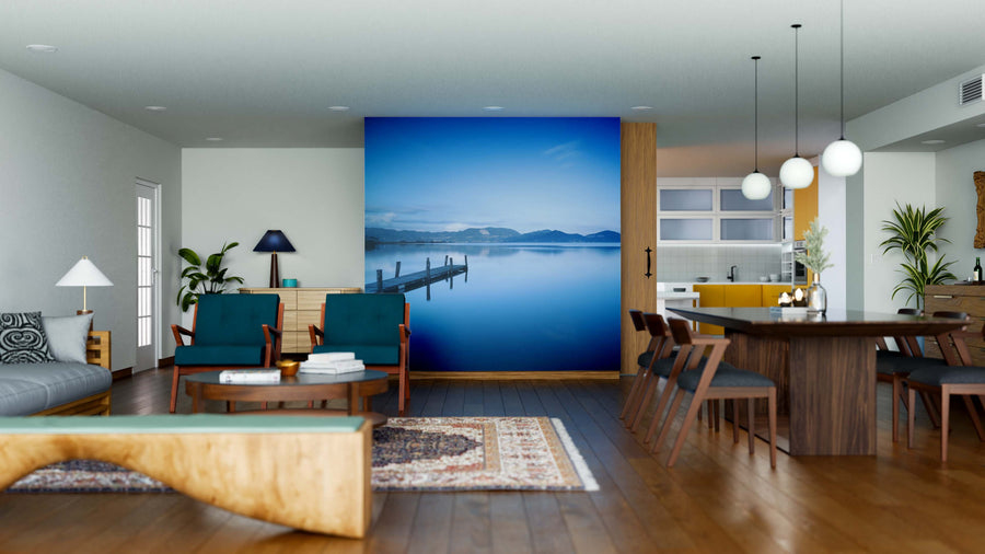 Modern open-plan living and dining area with wood floors and stylish furniture, featuring the Blue Lake Sunset Wall Mural as a focal point. The kitchen includes pendant lights, yellow accents, plants, and decorative touches throughout.
