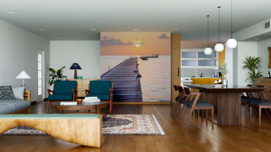 A modern open-plan living and dining room with wooden floors, teal chairs, and a dining table features the Island in Indian Ocean Wall Mural as a stunning focal point, complemented by plants, pendant lights, and an adjoining kitchen area.