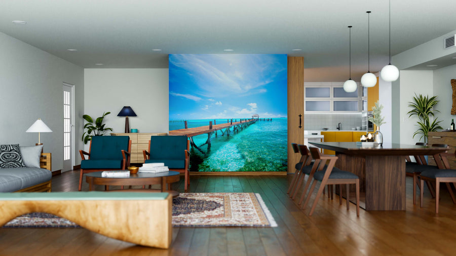 Modern open-plan living and dining room with wood floors, stylish furniture, and the Pier Into Paradise Wall Mural—featuring a tropical pier over turquoise waters under a blue sky—for an easy-to-update, vibrant, relaxing atmosphere.
