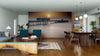 Modern living and dining area with wood floors, teal armchairs, and a large Sunbound Wall Mural of a sunset over a pier. Contemporary wooden furniture, globe pendant lights, rugs, and decor add warmth to the open space.