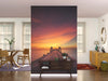 A modern living room with white walls features the Sunset Over Pier Wall Mural, showcasing a wooden pier at sunset. The space includes a wooden console table, dining area with chairs, round mirror, and large windows with sheer curtains.
