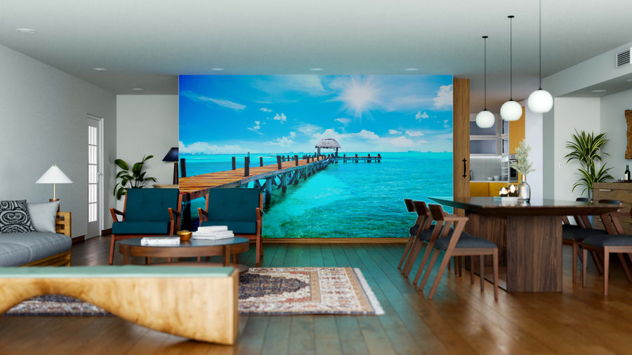 Modern living and dining area with wood floors and mid-century furniture; the Tropical Horizon Wall Mural features a vivid tropical pier extending into turquoise water under a sunny sky, creating an ocean view illusion indoors.