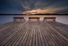 Enhance your space with the Photo "Pier and Benches Wall Mural," featuring a tranquil lakeside sunset with dramatic clouds and a colorful horizon, reflecting on smooth water. The wide wooden dock with benches offers a serene view, perfect for peel-and-stick installation.