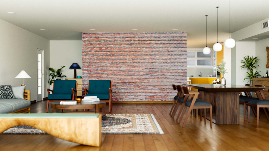 A modern open-plan living and dining area features a Pink Brick Wall Wall Mural accent, wooden floors, mid-century chairs with teal cushions, a wooden coffee table, large dining table beneath pendant lights, gray sofa, green plants, and sunlight from tall windows.