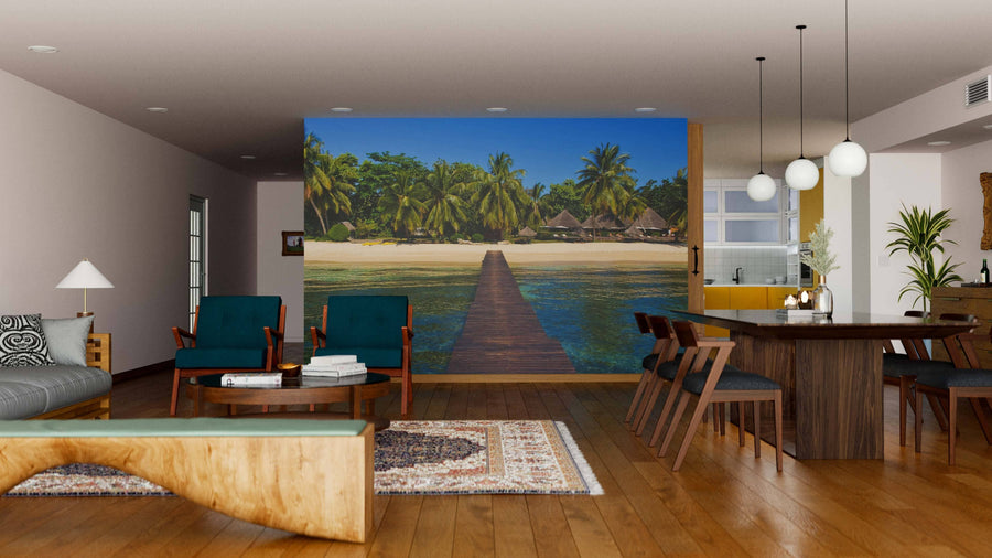 A modern living-dining space with wooden floors, green chairs, a low coffee table, and dining set is enhanced by the Pontoon Beach and Resort Wall Mural, depicting a sunny beach with palm trees and huts for an open, breezy feel.