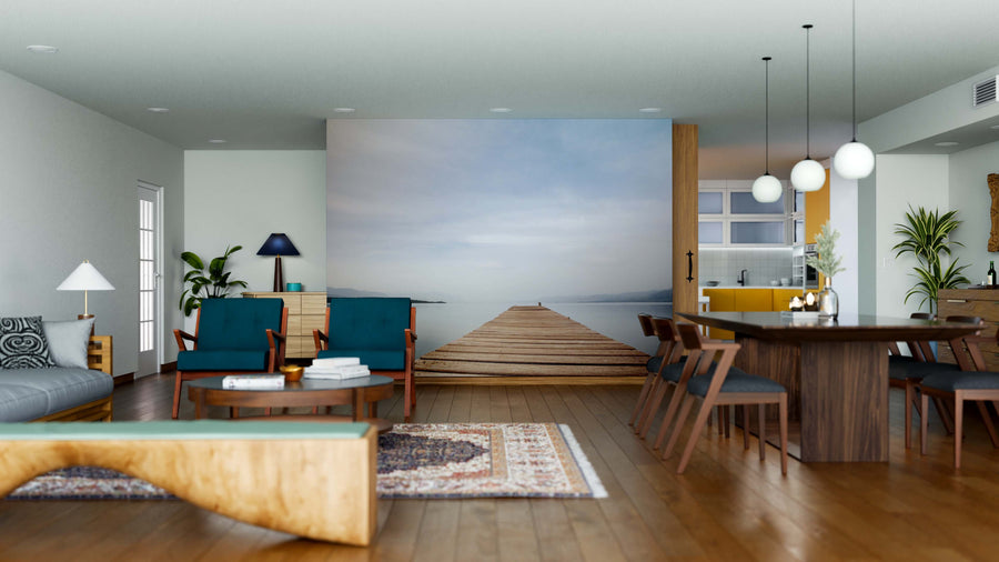 A modern open-plan living and dining area features wooden floors, blue chairs, a gray sofa, a six-seater dining table, and globe pendant lights. The Quiet Morning Dock Wall Mural adds a serene touch with its pier stretching into calm water.